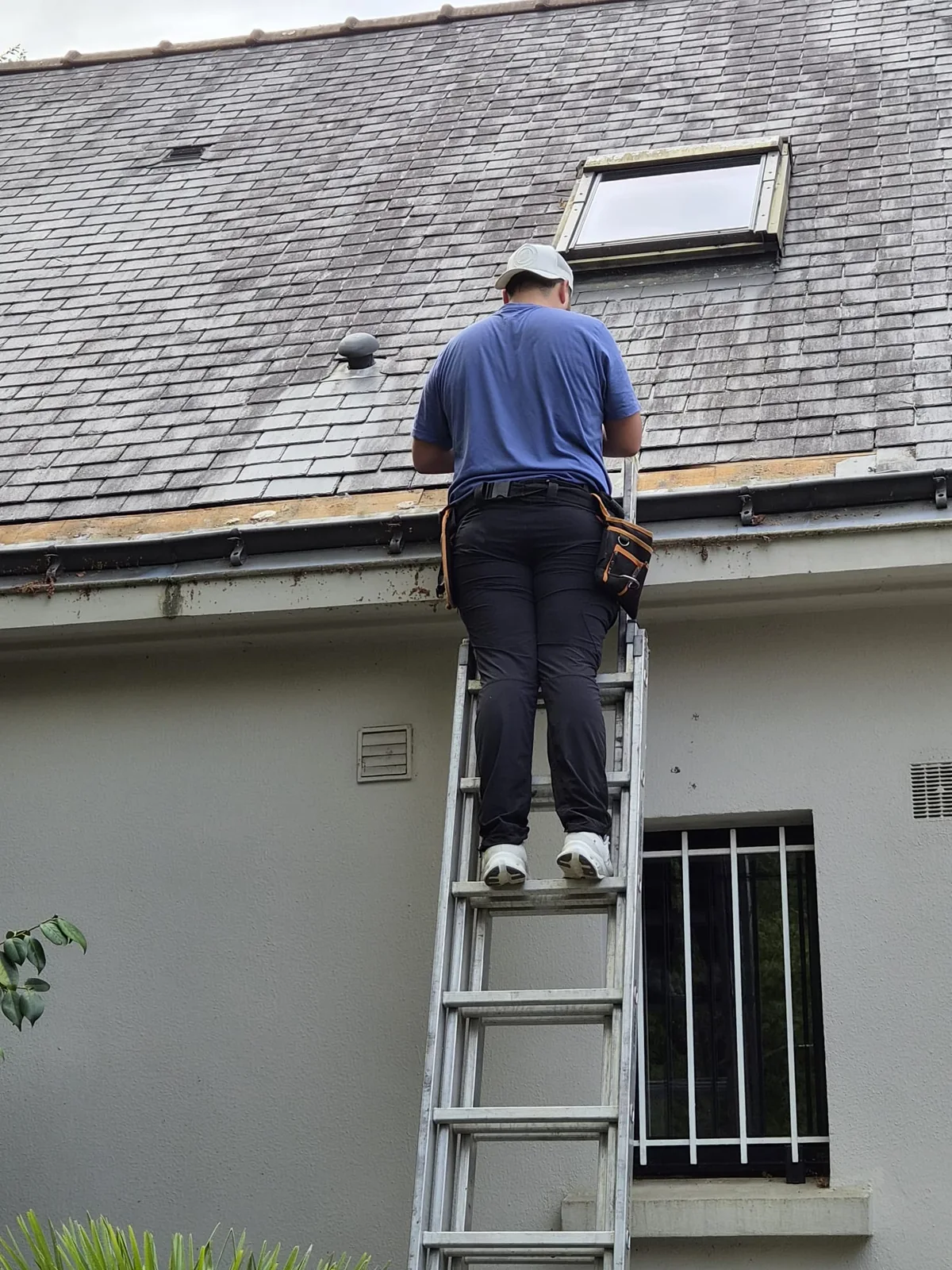 Artisan intervenant au bas d’une toiture en ardoises, près de la gouttière